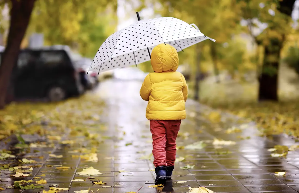 Little girl with umbrella walking together through a park